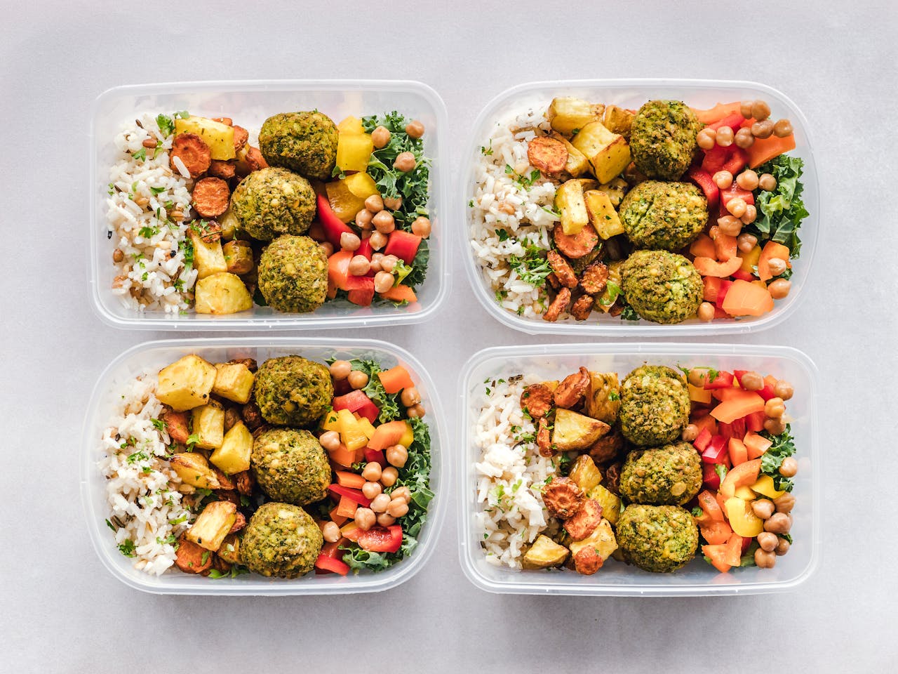 hero-img-01 Colorful meal prep containers with falafel, chickpeas, rice, and vegetables for a healthy lifestyle.