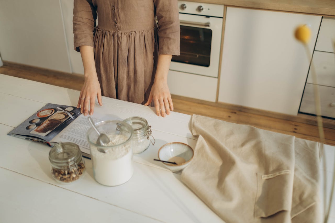 gallery-1 A person prepares ingredients on a wooden kitchen table with a cookbook for baking.