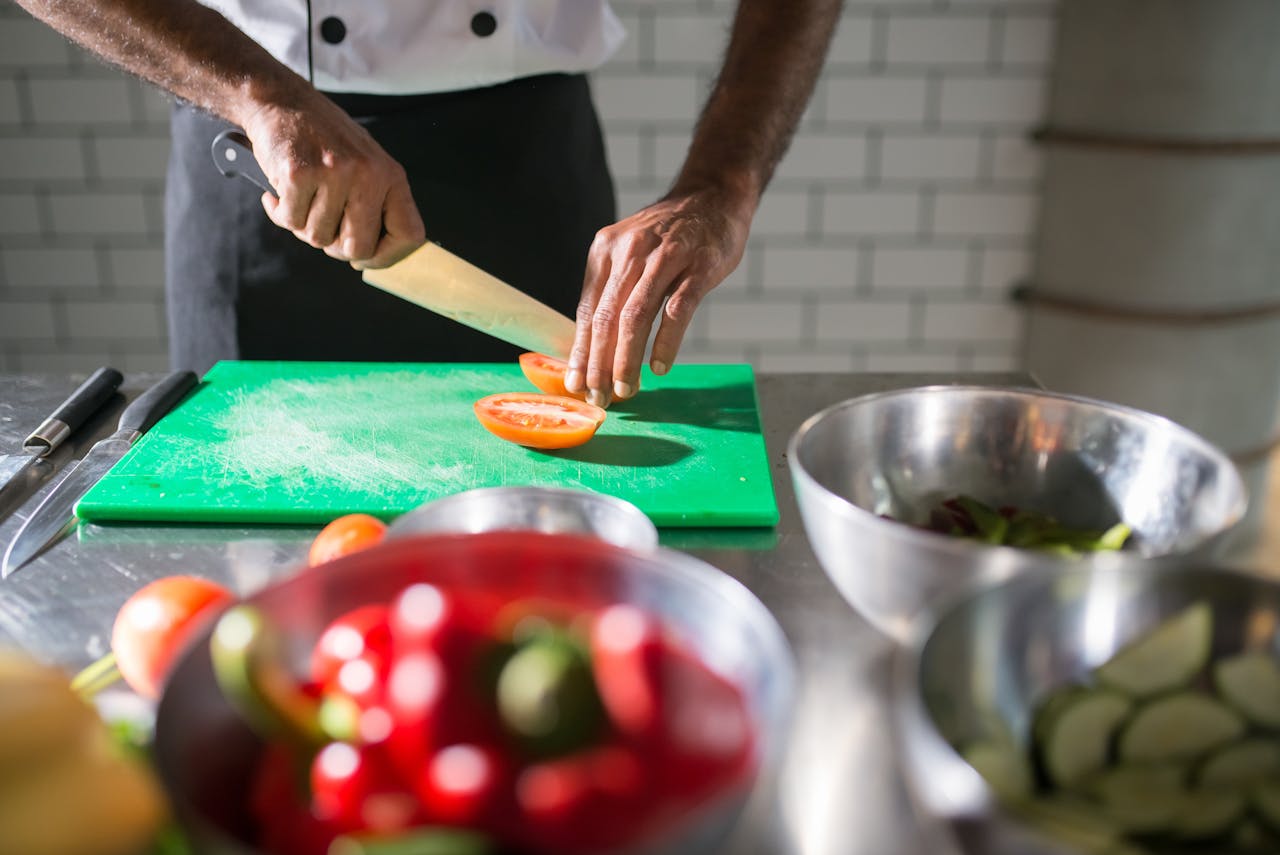 our-services-3 Chef skillfully slicing tomatoes on a chopping board in a commercial kitchen, highlighting culinary preparation.